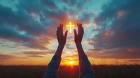 Silhouette of raised hands reaching toward glowing cross against dramatic sunset sky with vibrant orange and teal clouds over peaceful countryside landscape.