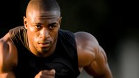 Athletic African American man in black shirt performing push-up exercise with intense focus and determination during fitness training workout routine.