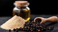 Ground black peppercorns and whole black pepper with wooden scoop on dark stone surface next to glass jar with olive oil, moody food photography.