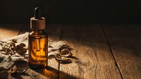 Amber glass dropper bottle with golden oil on rustic wooden surface with coffee beans and burlap sack for natural skincare and aromatherapy products.