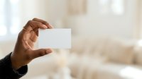 Close-up of male hand holding blank white business card against blurred office background for corporate branding and contact information display.