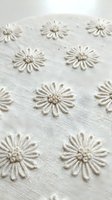 White embroidered daisy flowers on natural linen fabric texture creating elegant floral pattern for home decor and fashion design projects.