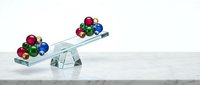 Colorful glass balls on a tilting transparent scale on marble surface, symbolizing imbalance, inequality, and decision-making concepts.