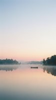 Serene dawn landscape with solitary boat on misty lake surrounded by forested shoreline, soft pastel sky reflecting on calm water for peaceful nature and travel concepts.