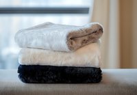 Stack of folded soft plush blankets in white, beige and black colors on sofa, cozy home textile and interior decor for comfortable living space.