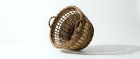 Handwoven wicker basket tilted on white surface showing natural brown rattan texture and traditional craftsmanship for home decor and storage solutions.