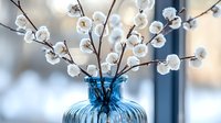 White cotton stems arranged in blue glass vase against soft blurred background. Farmhouse style home decor with natural dried flowers creates cozy atmosphere.