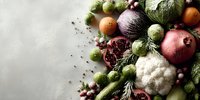 Fresh seasonal vegetables and fruits arranged on light background, including cauliflower, brussels sprouts, pomegranate, and citrus for healthy eating concept.