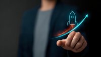 Glowing blue rocket icon launches upward along rising graph curve against dark background, symbolizing business growth and startup success. Professional points at digital display.