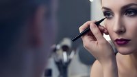Young Caucasian woman applying black eyeliner pencil in mirror, dark berry lips, glamour makeup routine for beauty and fashion concepts.