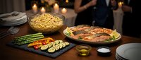 Festive dinner table with roasted chicken, grilled vegetables, and side dishes in warm restaurant setting with bokeh lights for holiday celebrations.
