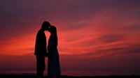 Romantic couple silhouette embracing at sunset with dramatic orange and purple sky. Love, romance, relationship concept for wedding, anniversary designs.