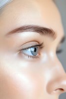 Close-up view of bright blue eye with long eyelashes and perfectly shaped eyebrow showing natural beauty makeup and flawless skin texture.