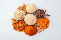 Assorted healthy grains, legumes, nuts and spices including quinoa, lentils, almonds, chickpeas and red chili powder arranged on white background.