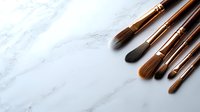 Professional makeup brushes with rose gold ferrules arranged on white marble background, essential tools for beauty artists and cosmetic application.