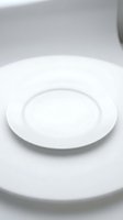 Empty white ceramic dinner plate on clean white surface with soft lighting for food photography and kitchen design mockups.