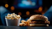 Crispy chicken burger with sesame bun and french fries in white paper container on dark background with blurred bokeh lights creating cozy atmosphere.