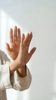Two female hands pressed against glass surface with natural sunlight creating shadows and reflections in minimalist setting for wellness concepts.