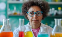 African American female scientist with afro hair and blue glasses in laboratory setting surrounded by colorful liquid-filled flasks, wearing white coat and pink shirt.