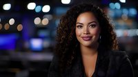 Young African American businesswoman with curly hair and confident smile against blurred city lights background, wearing black blazer for professional headshot.