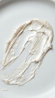 Creamy white cosmetic product with thick, luxurious texture spread on neutral background, suitable for skincare, beauty, and wellness marketing materials.