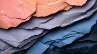 Layered colorful cosmetic texture with smeared cream product samples in coral pink, gray and blue tones creating abstract waves and patterns.