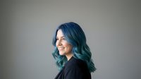 Young woman with vibrant blue-green hair smiling in profile against neutral background for beauty and fashion concepts.
