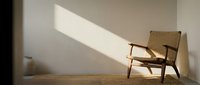 Wooden mid-century modern chair positioned against white wall with natural sunlight casting geometric shadows, minimalist interior design concept for home decor and furniture styling.