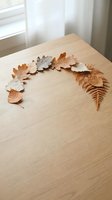 Paper cut autumn leaves and fern arranged in curved line on wooden table near window with natural light for seasonal crafting projects.