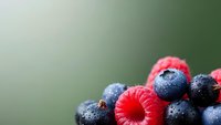 Fresh mixed berries with water droplets on blurred green background for healthy eating and nutrition concepts.