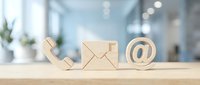 Wooden contact icons phone envelope email symbol on desk in modern office interior for business communication and customer service concepts.