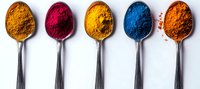 Vibrant colorful spices in silver spoons arranged in row on white background - turmeric, sumac, curry, indigo and paprika powders for cooking and natural food coloring.
