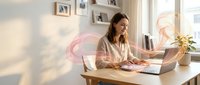 Young professional woman working on laptop at modern home office desk with natural lighting and minimalist decor for remote work productivity.