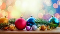Colorful Christmas ornaments and pine branches arranged on wooden surface with festive bokeh background in rainbow colors.