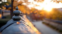 Zen stones balanced in pyramid with small blue bird on top against golden sunset background, autumn leaves scattered around creating peaceful meditation scene.