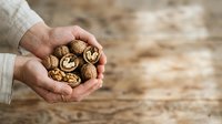 Male hands holding cracked walnuts on wooden surface. Suitable for food, nutrition, healthy eating, agriculture, and organic product marketing materials.