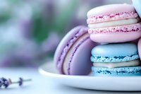 Colorful French macarons in pastel pink, purple, and blue stacked on white plate with soft bokeh background, close-up view showing delicate texture and filling.