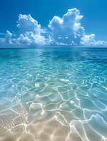 Tranquil turquoise ocean water with light ripples over sandy bottom and dramatic white cumulus clouds in bright blue sky, creating serene tropical seascape.