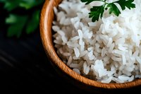 Steamed white jasmine rice in wooden bowl garnished with fresh parsley leaf, close-up view on dark background for food photography and menu design.