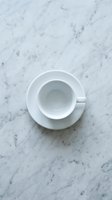 Empty white ceramic cup and saucer on marble surface, overhead view. Minimalist tableware composition for beverage, coffee, tea, or kitchen design projects.