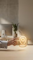 Hand of person in business attire pointing at glowing location pin icon on wooden desk in modern office workspace with potted plant and computer monitor in background for navigation and GPS concepts.