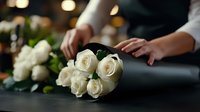 Fresh white roses bouquet on dark background with female hands arranging flowers, soft bokeh lights create romantic atmosphere for wedding or celebration.