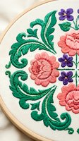 Colorful floral embroidery hoop with pink roses, purple violets and green leaves on white fabric for needlework crafts and textile art projects.