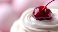Fresh ripe cherry on top of white whipped cream swirl against soft pink background, macro food photography with selective focus and bokeh effect.