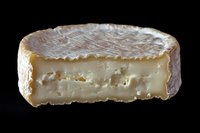 Creamy soft ripened cheese with white mold rind cut in half showing smooth interior texture and characteristic holes against dark background.