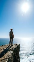 Woman in casual outdoor attire standing on rocky cliff overlooking sparkling ocean waters under bright sunlight, representing adventure, exploration, and freedom for travel and lifestyle content.