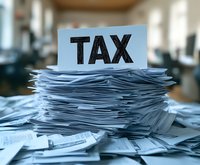 Large pile of tax documents and paperwork with TAX sign on top in office setting for accounting and financial preparation during tax season.