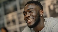 Young African American man with beard smiling broadly outdoors in urban setting. Casual lifestyle portrait showing genuine happiness and positive energy.