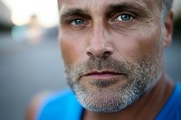 Close up portrait of mature Caucasian man with gray beard and striking blue eyes wearing blue shirt, looking confidently at camera with natural lighting and shallow depth of field.