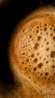 Rich coffee foam with golden bubbles and creamy texture against dark background for beverage advertising and cafe marketing materials.